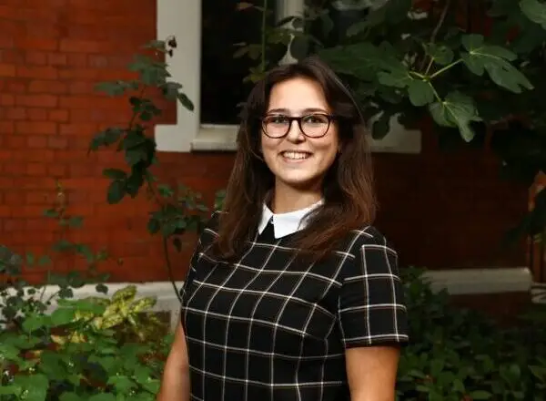 Charis Almond, female with brown hair and glasses in checked dress with white collar.